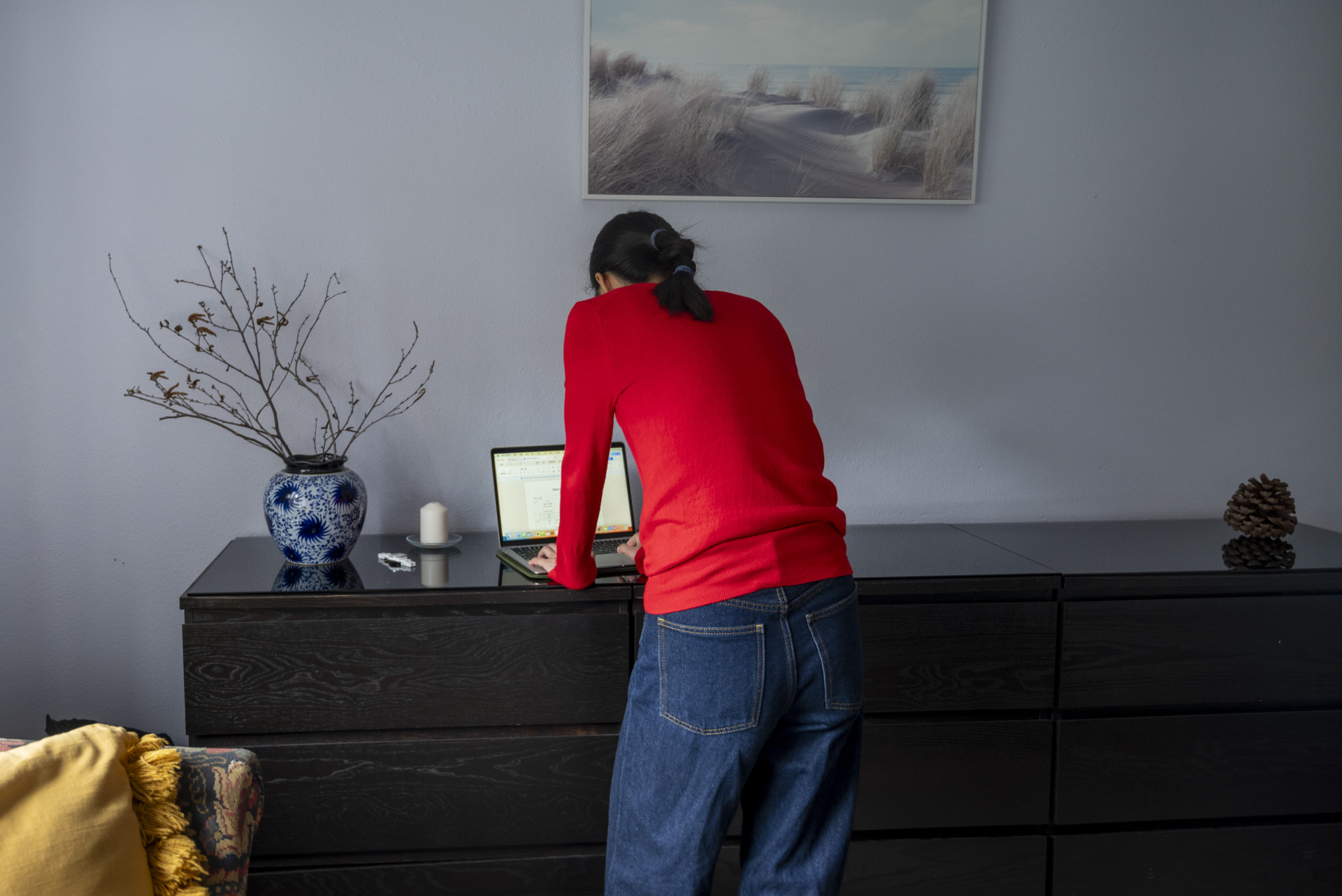 Ling, works on her laptop in a cabinet in her bedroom. She assists her husband by managing visa-related documents and organising files. Ling collected the decorative branches in the vase on the cabinet from a nearby park.