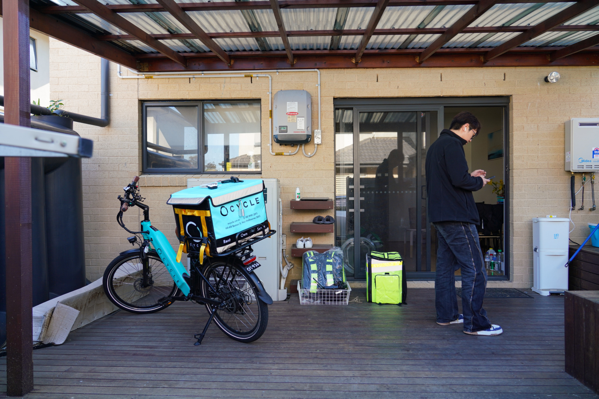 Yang Xihan stands next to his delivery bike while checking his phone in Clayton, Melbourne on October 2, 2024. Like many young people in this area, he juggles multiple jobs, delivering food and repairing e-bikes at a local workshop, all while pursuing his own dream. &ldquo;I check the delivery app to find the best orders,&rdquo; Yang says.