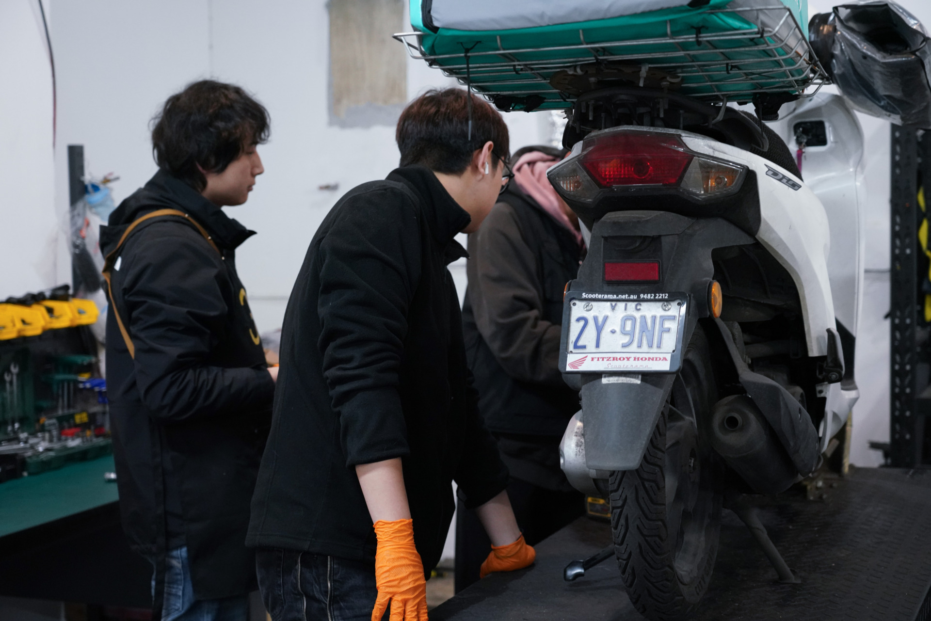 Yang Xihan and his colleagues inspect a scooter at their workshop in West Melbourne on October 2, 2024. Three mechanics huddle around the bike, a scene during their busy repair days. &ldquo;We just clicked during our chat. When I mentioned my previous experience fixing e-bikes, they let me try some repairs,&rdquo; Yang says.