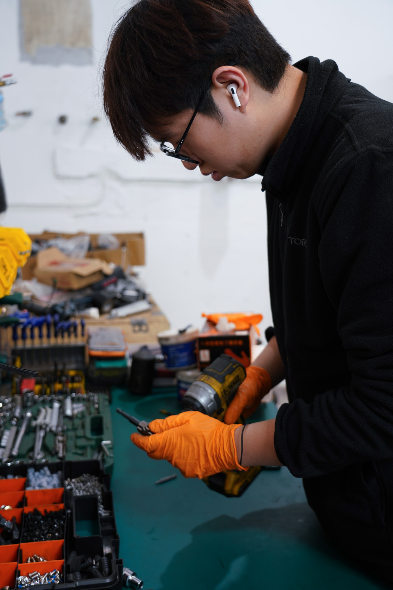 Yang Xihan works at his repair bench in West Melbourne on October 2, 2024, his orange gloves gripping repair tools amid boxes of spare parts. His AirPods and focused expression show his concentration at work. &ldquo;At first, I couldn&rsquo;t even tell the difference between a controller and an inverter,&rdquo; he says with a laugh. The small workshop, squeezed between a cafe and boutique shop, buzzes with the sound of repairs throughout the day.