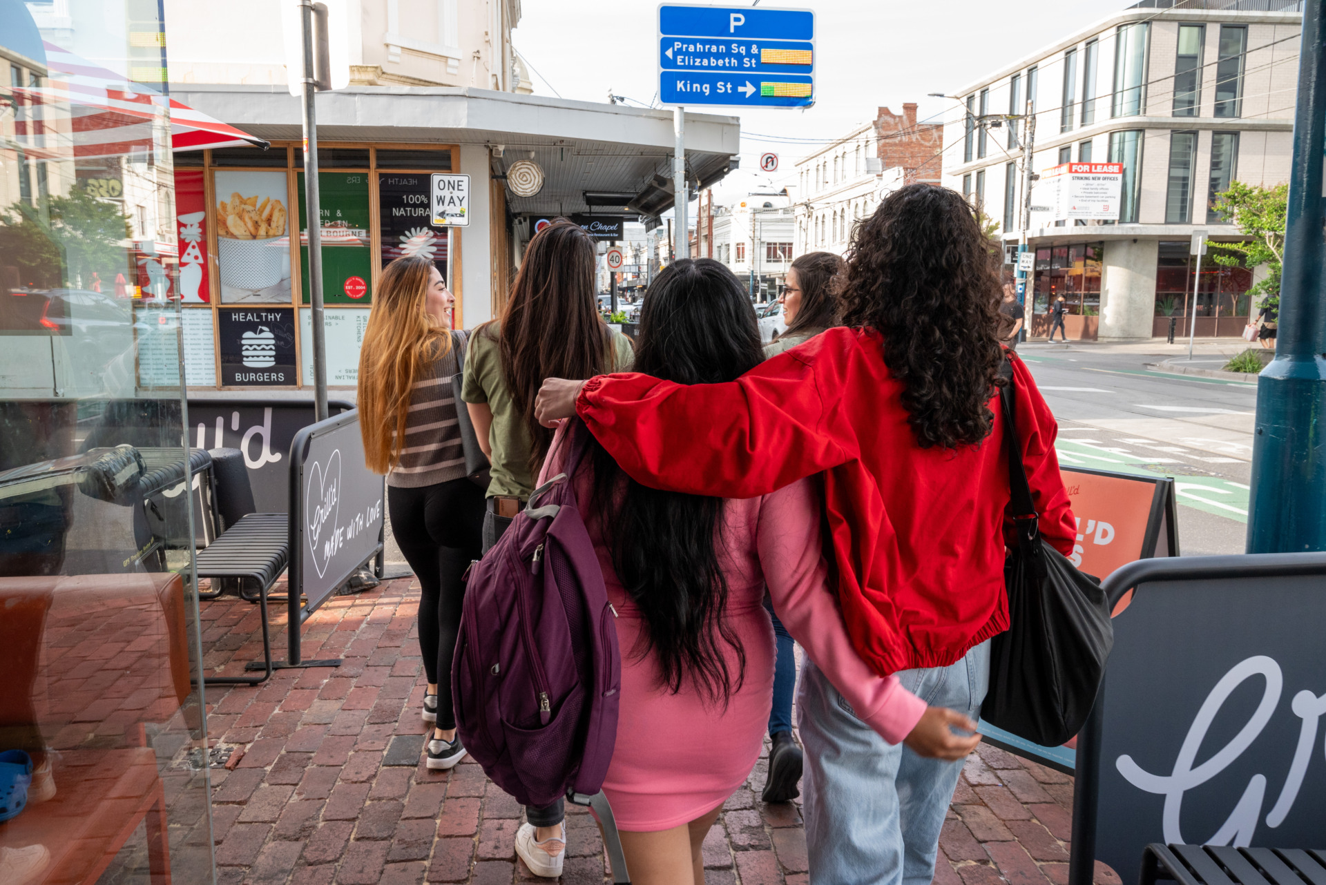 After dinner, organiser Carolina hugs Diana as they stroll through the streets of St Kilda with other members, discussing which dessert shop to visit for ice-cream. They walk and chat, enjoying the warm and relaxed atmosphere in this artistic district.