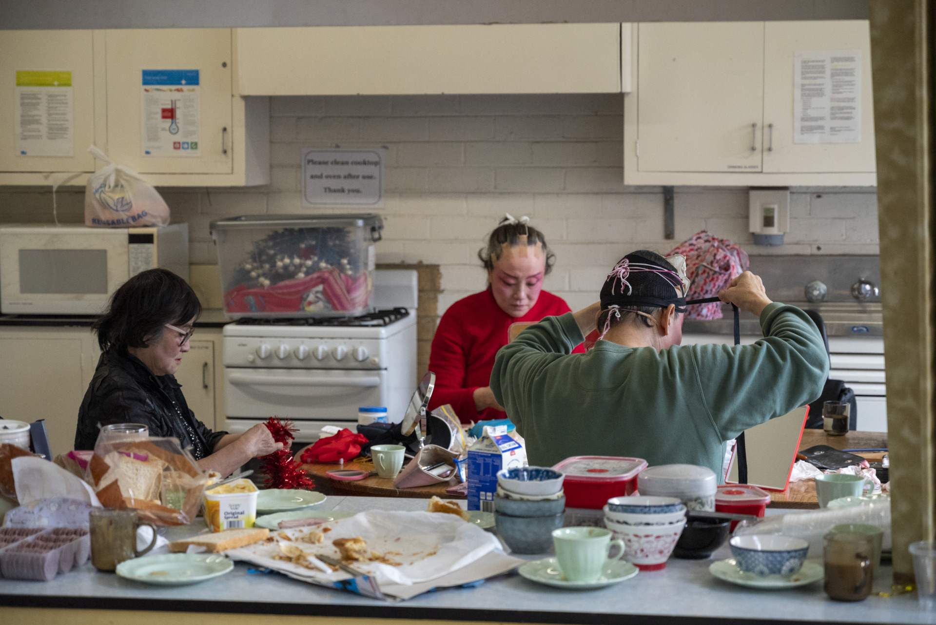 Guofen Tu of Harmony Peking Opera Group prepares costumes as actors Huimin Li and Min Chen put on their costumes in the church kitchen in Footscray, Melbourne, in the lead-up to the show. Make sure the actors are in good condition before going on stage and that the costumes are correct.