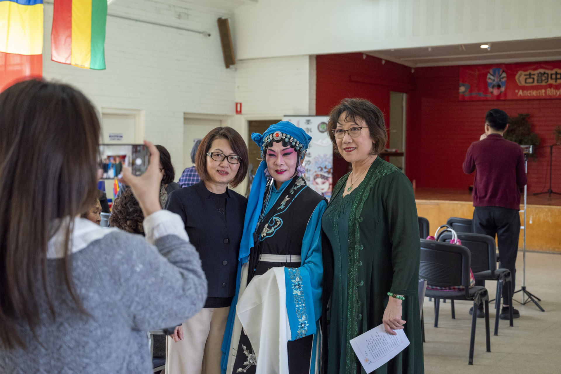 1:00pm Before the start of the performance, Peking Opera actress Yingbao Hu of Harmony Peking Opera Group took a photo with two audience members at Footscray Church. Dressed in her opera costume, she smiled warmly at the camera, while the audience members appeared thrilled and delighted. This moment highlights the interaction between the actors and audience, capturing the harmonious and lively atmosphere of the Mid-Autumn Festival celebration.