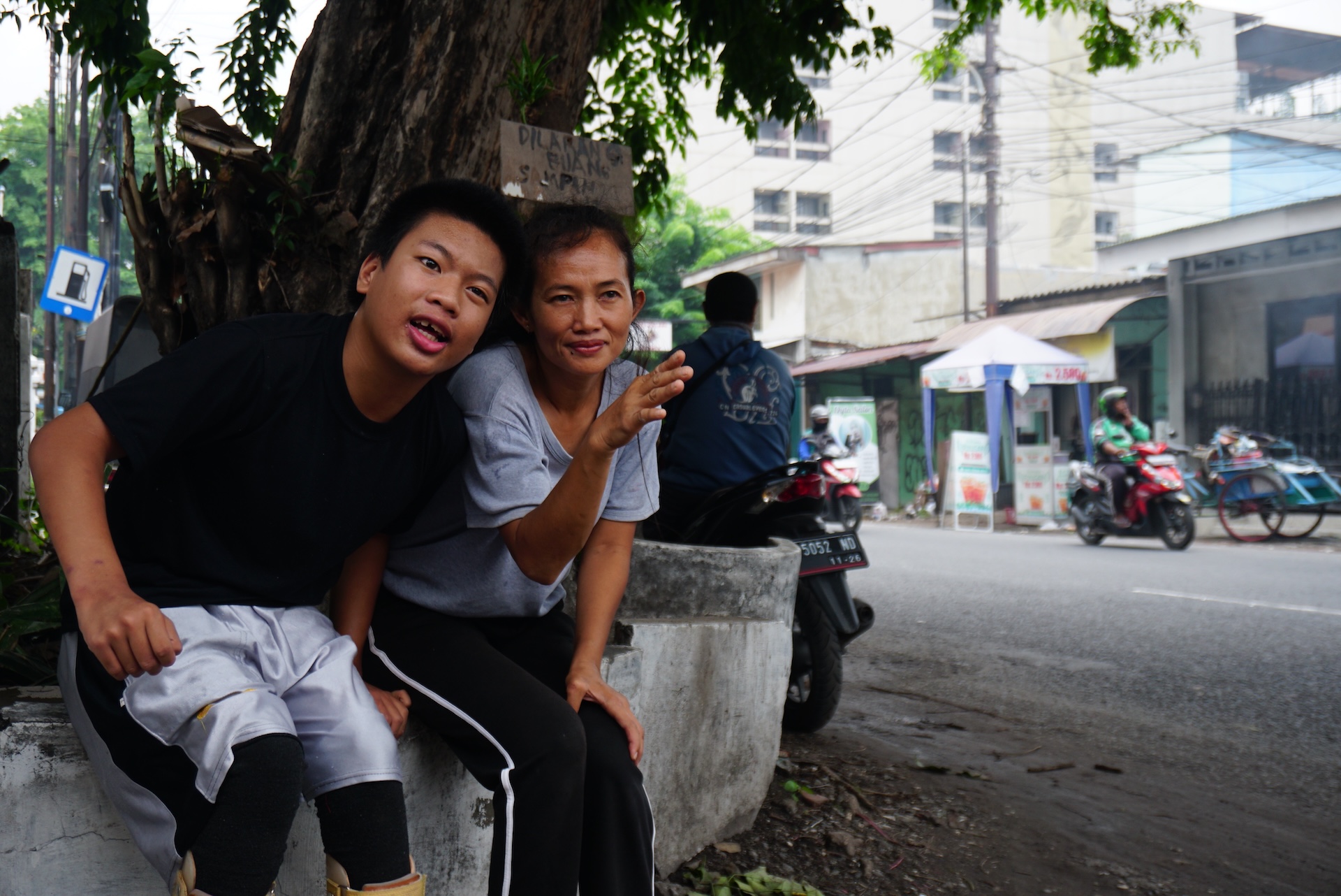Carer Ayung Tarunawati sits with Jonathan, who cerebral palsy, to watch the passing cars on the road outside the neighborhood of Dinoyo in Surabaya, Indonesia. Photo:Kristian Oka Prasetyadi