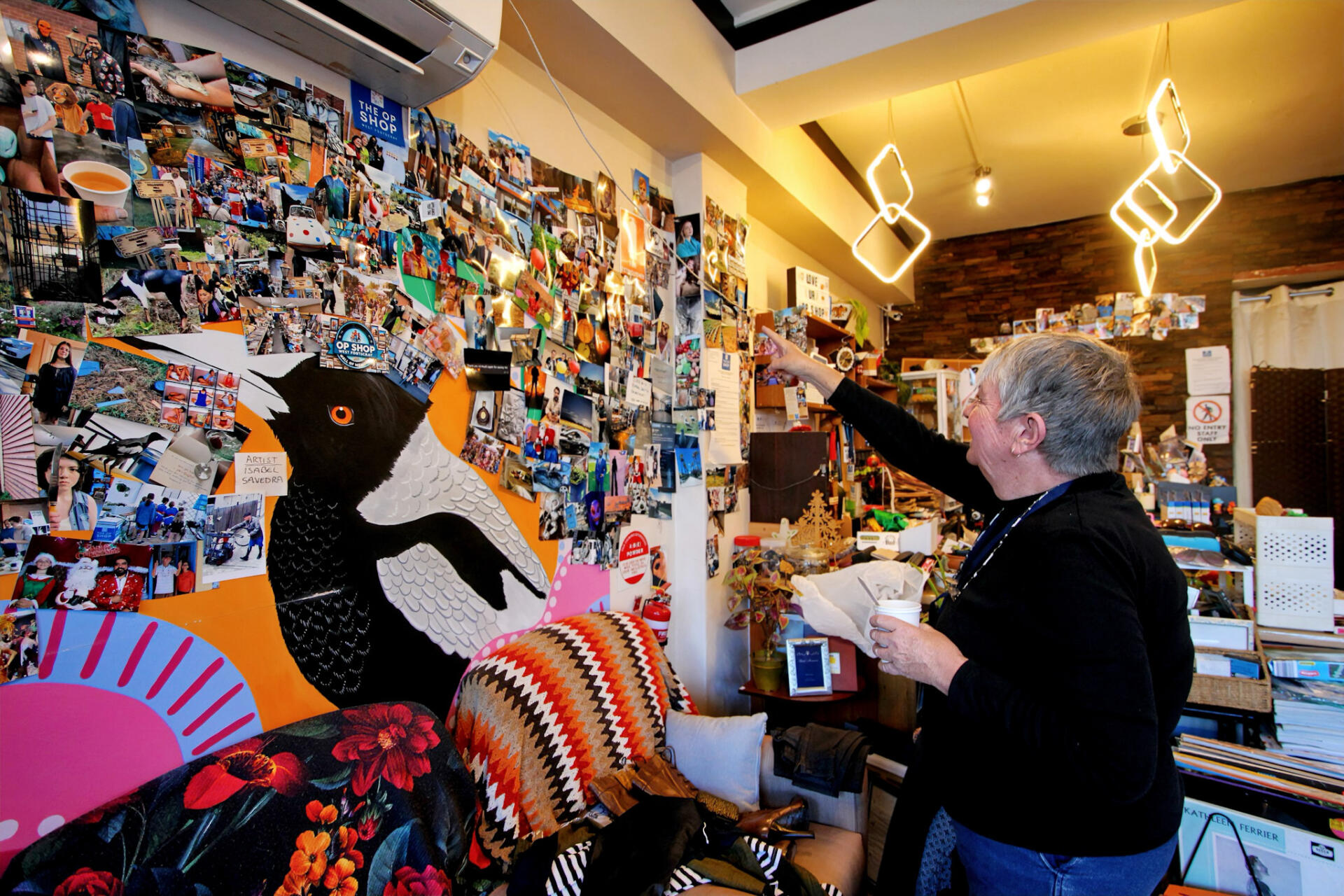 Staff member Tina Barrass explains the photo wall inside The Op Shop featuring thank-you letters, photos of sponsored children, and snapshots from past events.