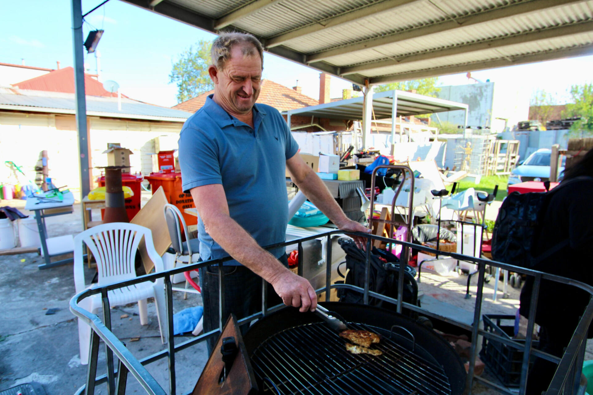 Volunteer and local farmer Kevin Martin leads a cheerful backyard gathering at The Op Shop, laughing as he grills and chats with the community.