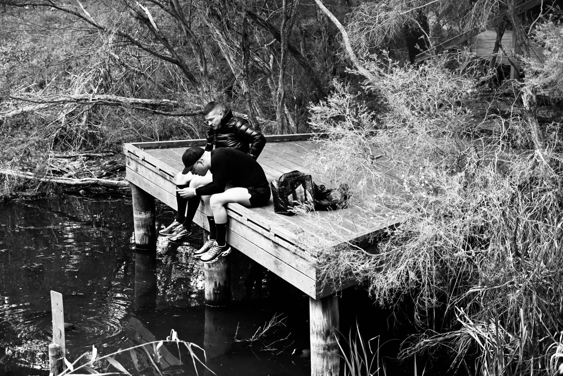 Two men sit on a pier overlooking a quiet inlet