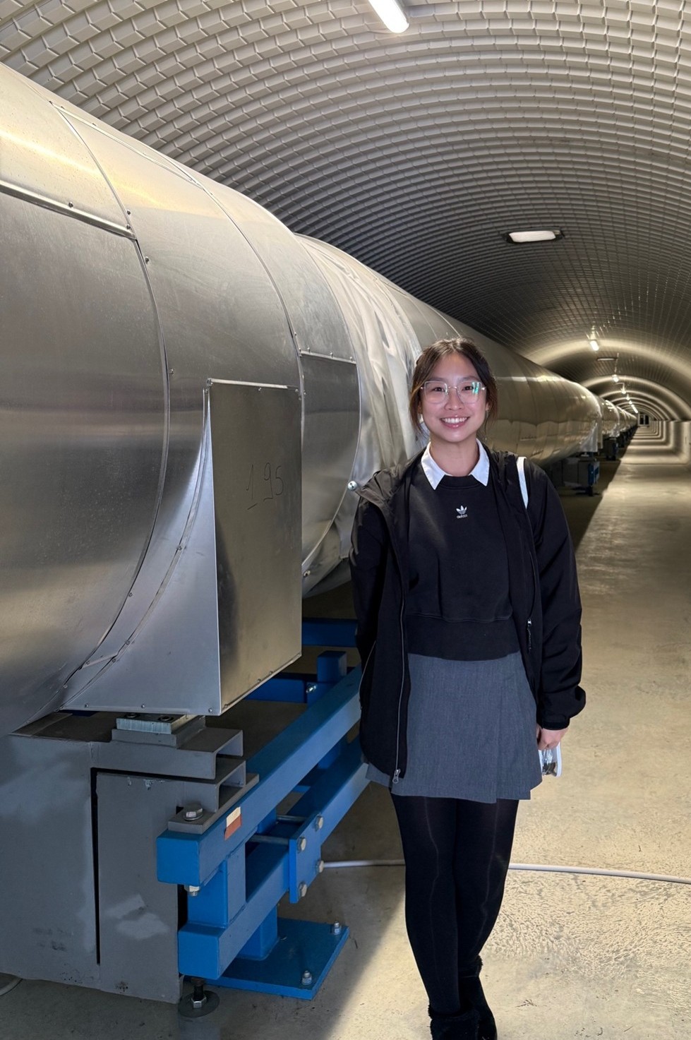 Christine Lee with the Virgo gravitational-wave detector in 2026. Virgo is one of the observatories used by scientists to search for gravitational waves from cosmic events. Photo: Supplied.