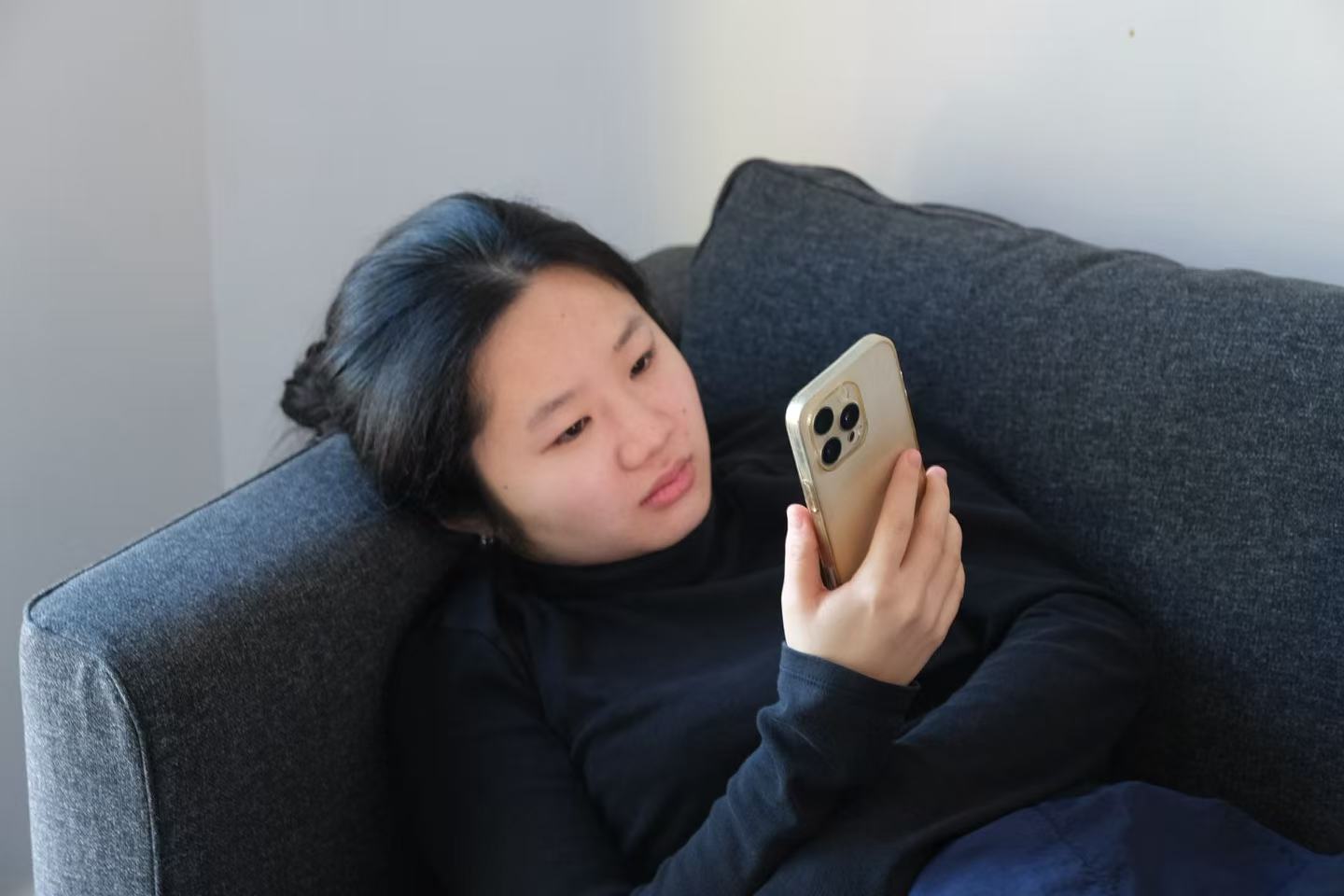 A woman looks at a phone while reclining on a sofa. Photo by Wanying Ou.